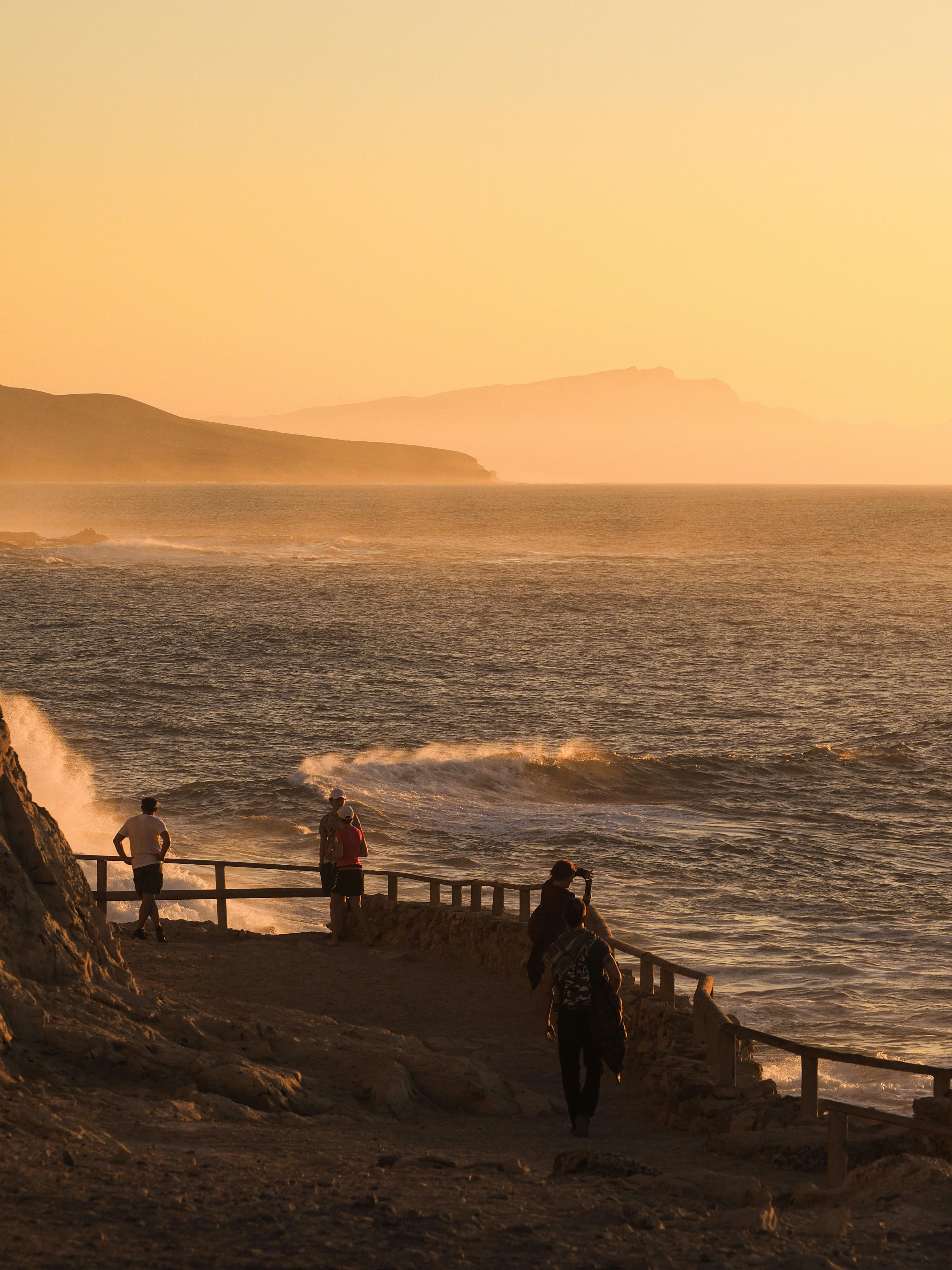 People enjoying a serene seaside walk during a breathtaking sunset with waves crashing.