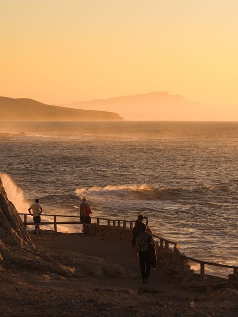 People enjoying a serene seaside walk during a breathtaking sunset with waves crashing.