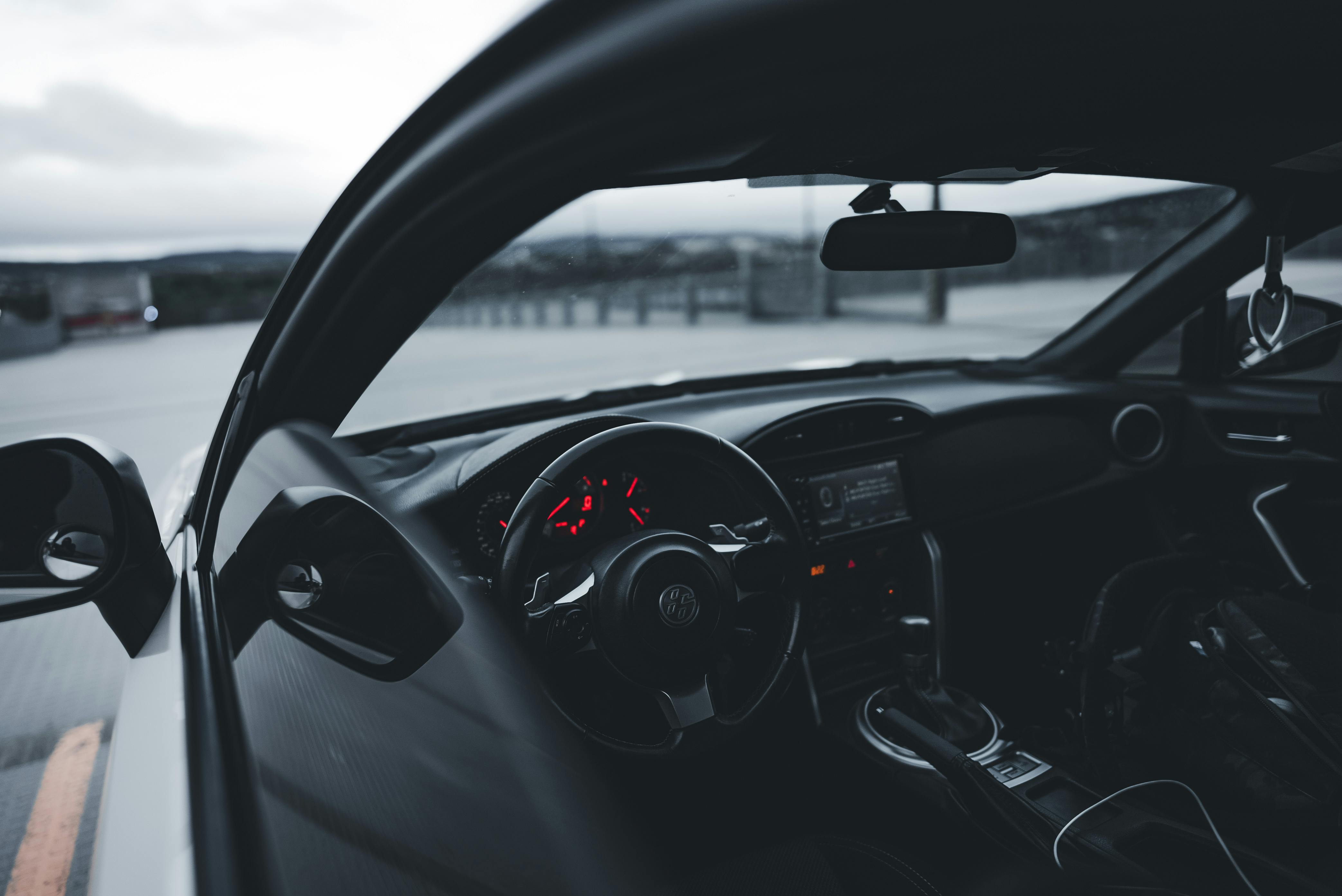 Close-up of a modern car interior featuring a sleek steering wheel and illuminated dashboard in an empty outdoor setting.