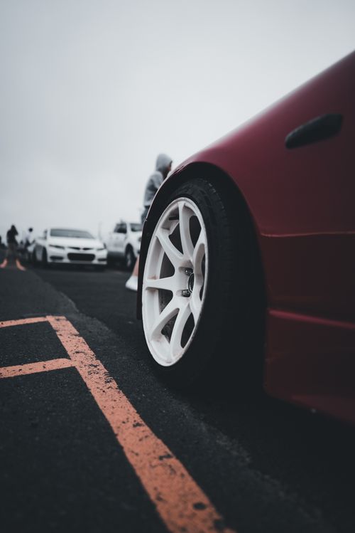 Free Close-up view of a red car's custom wheel with others parked in the background. Stock Photo
