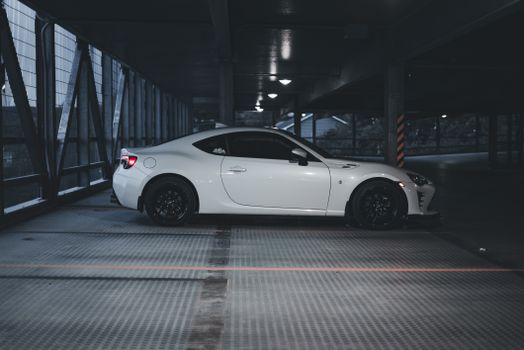 A sleek white sports car parked in an urban garage under low light conditions.