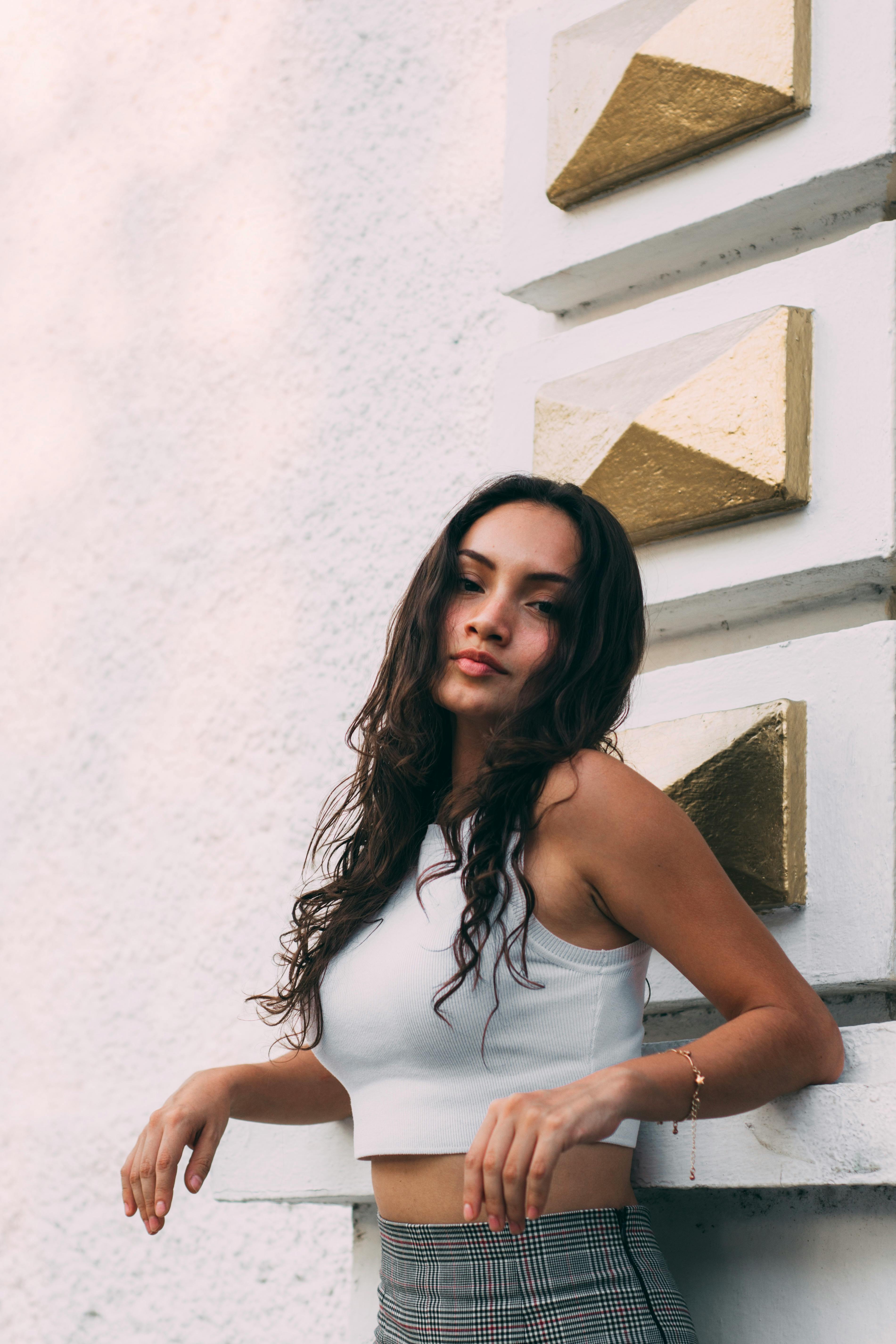 A fashionable woman in a white crop top posing against a textured wall with geometric designs.