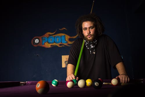 Man Standing next to a Pool Table with a Cue Stick 
