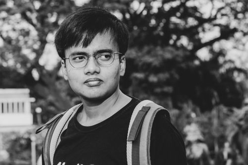 Free A thoughtful man with eyeglasses and backpack captured in a black-and-white portrait outdoors. Stock Photo