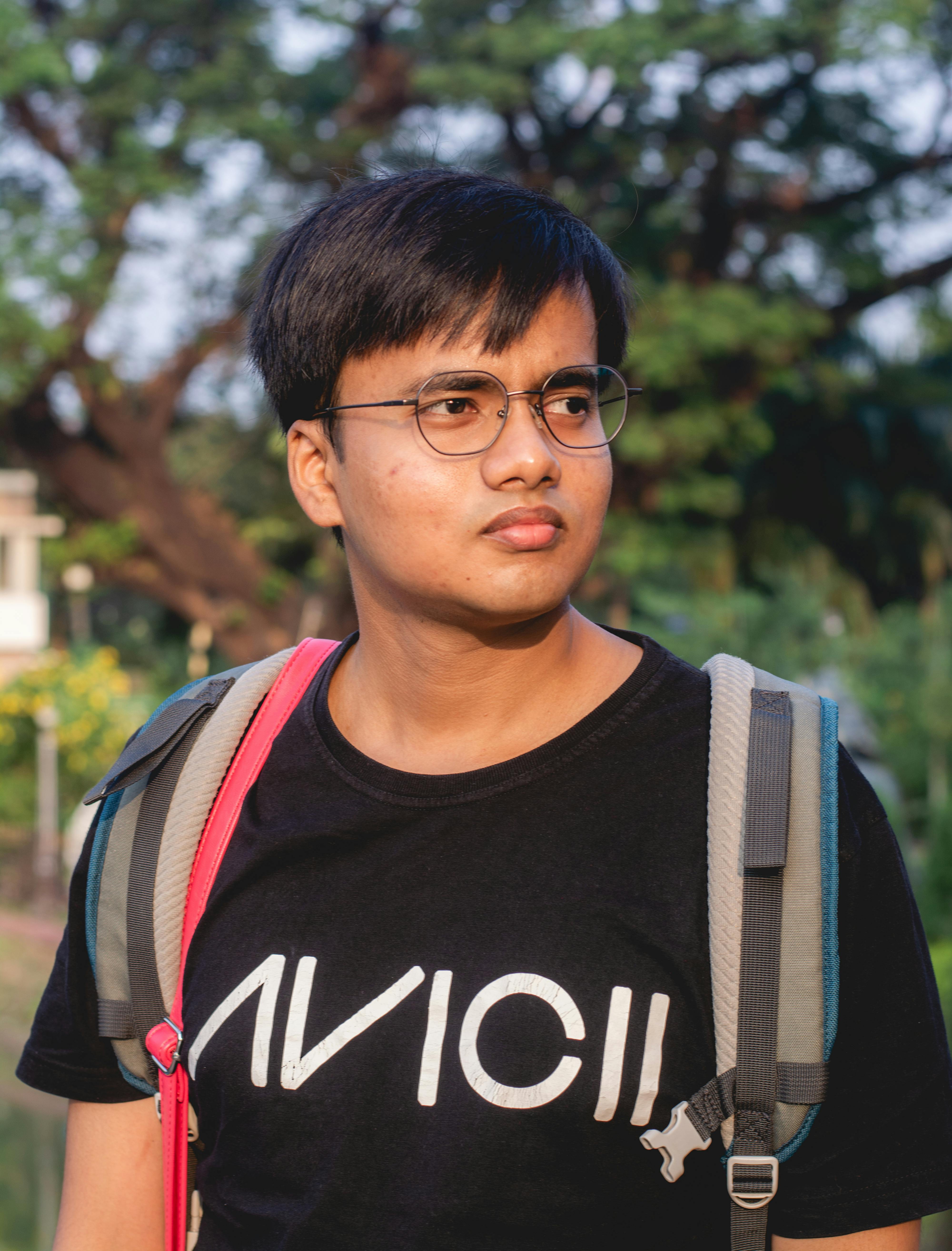 Portrait of a young man wearing glasses and a t-shirt outdoors with a backpack, captured during the day.