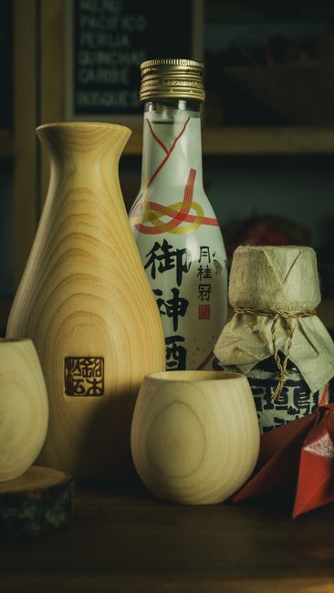 A clear glass bottle of sake next to a small ceramic cup, with a splash poured for cooking use.