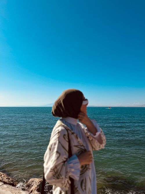 Free A woman in a hijab stands by the sea, enjoying the view on a sunny day. Stock Photo