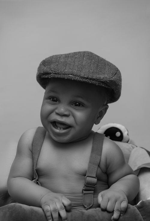 Free A joyful baby wearing a flat cap smiles warmly in this black and white portrait. Stock Photo