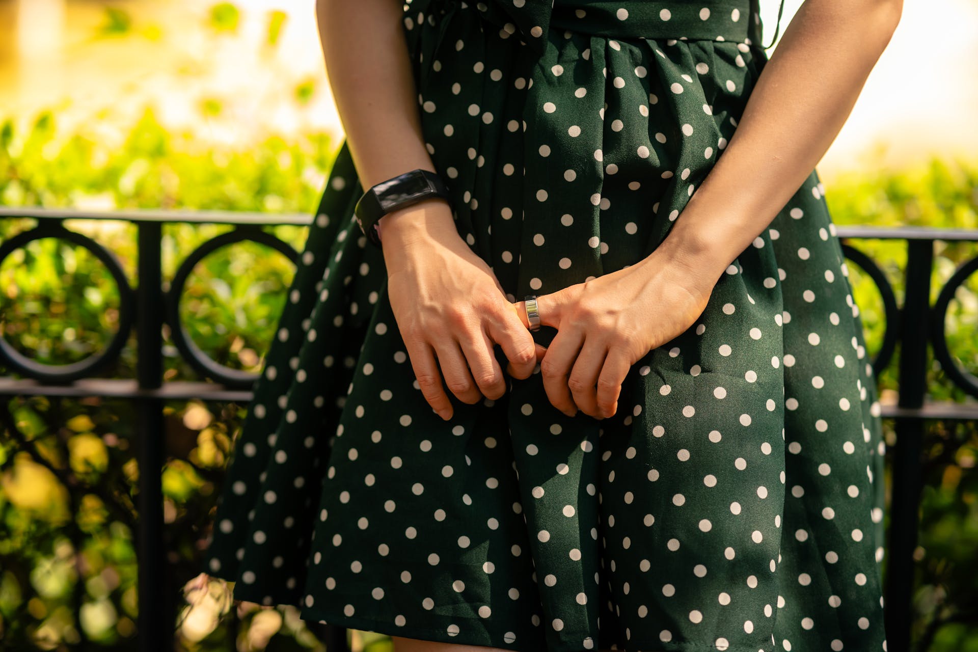 Close-up of a woman wearing a trendy green polka dot dress, showcasing her hands and bracelet.