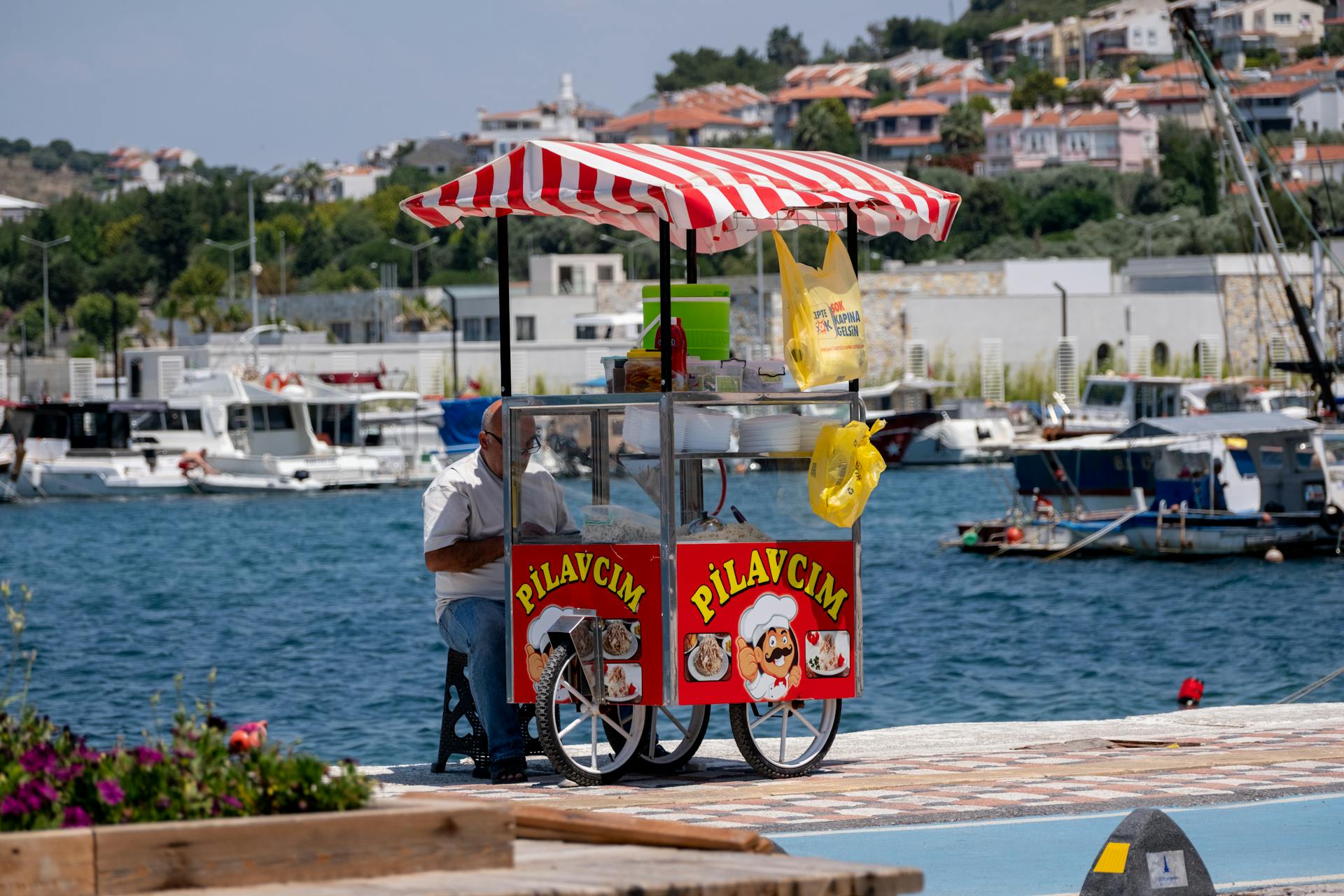 A street food vendor with a mobile cart at Foça Marina, showcasing a vibrant coastal town setting.