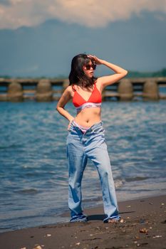 Fashion model posing confidently on the coastline in a red bikini, showcasing summer beach style.