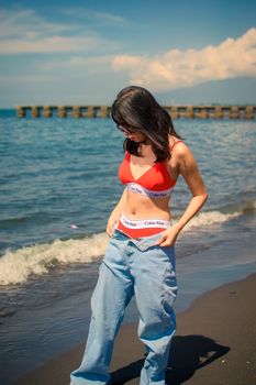Stylish woman on a sunny beach wearing a red bikini and jeans.