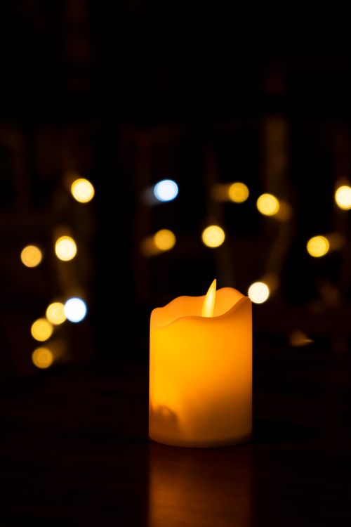 Free Close-up of a glowing candle with soft bokeh in the dark, creating a warm atmosphere. Stock Photo