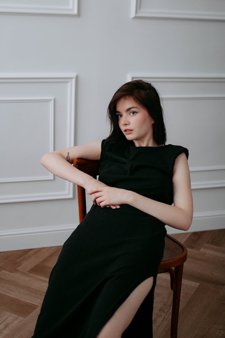 Beautiful Brunette Woman In Black Sleeveless Dress Sitting On A Chair