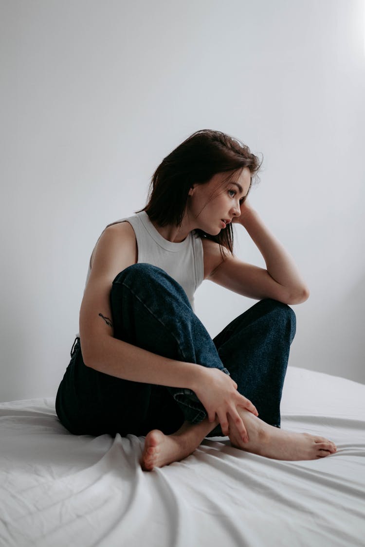 Woman Sitting On Bed With Crossed Legs And Leaning Head On Hand