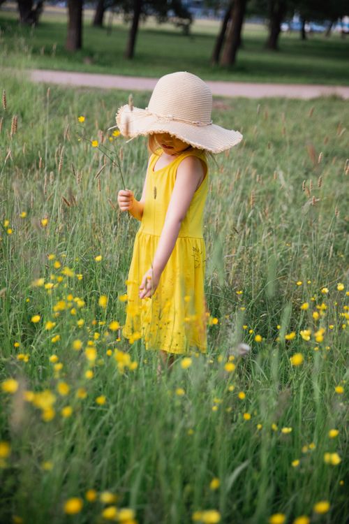 Free A child wearing a yellow dress and sun hat standing in a flower-filled rural area. Stock Photo
