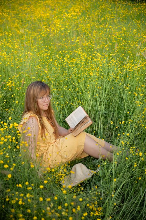 Free A woman in a yellow dress reads a book in a vibrant flower-filled meadow. Stock Photo