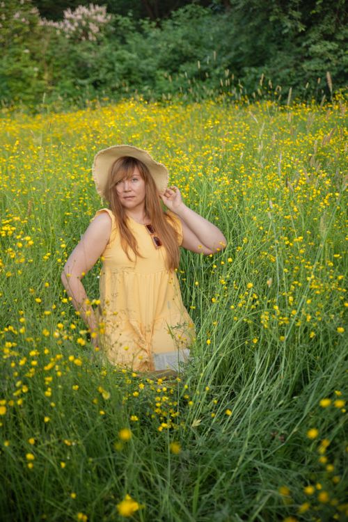 Free A woman wearing a yellow dress and hat stands amidst blooming wildflowers in a lush meadow. Stock Photo