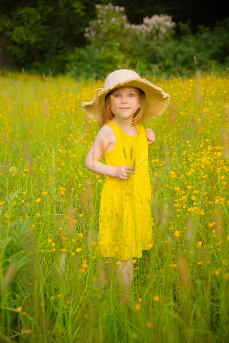 A Little Girl In A Yellow Dress And A Hat Standing On A Meadow With Yellow Flowers 