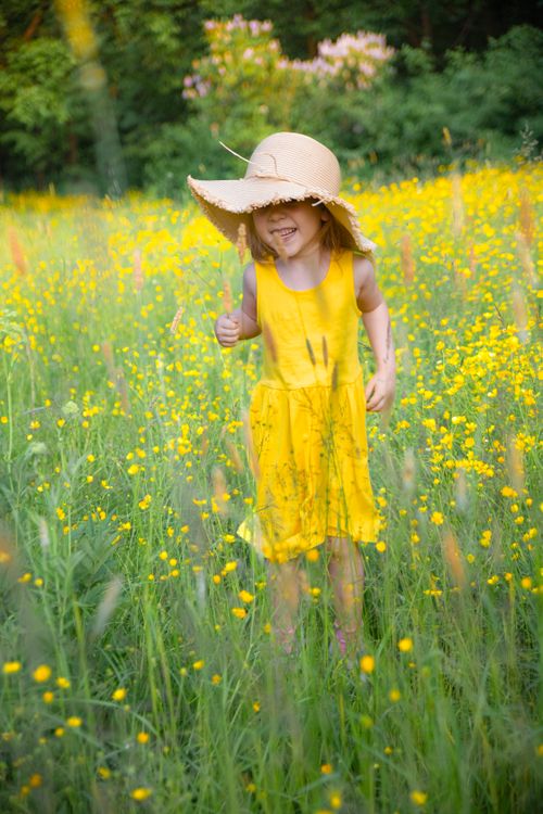 Free Smiling child in a yellow dress, standing in a meadow filled with flowers, enjoying a sunny day. Stock Photo