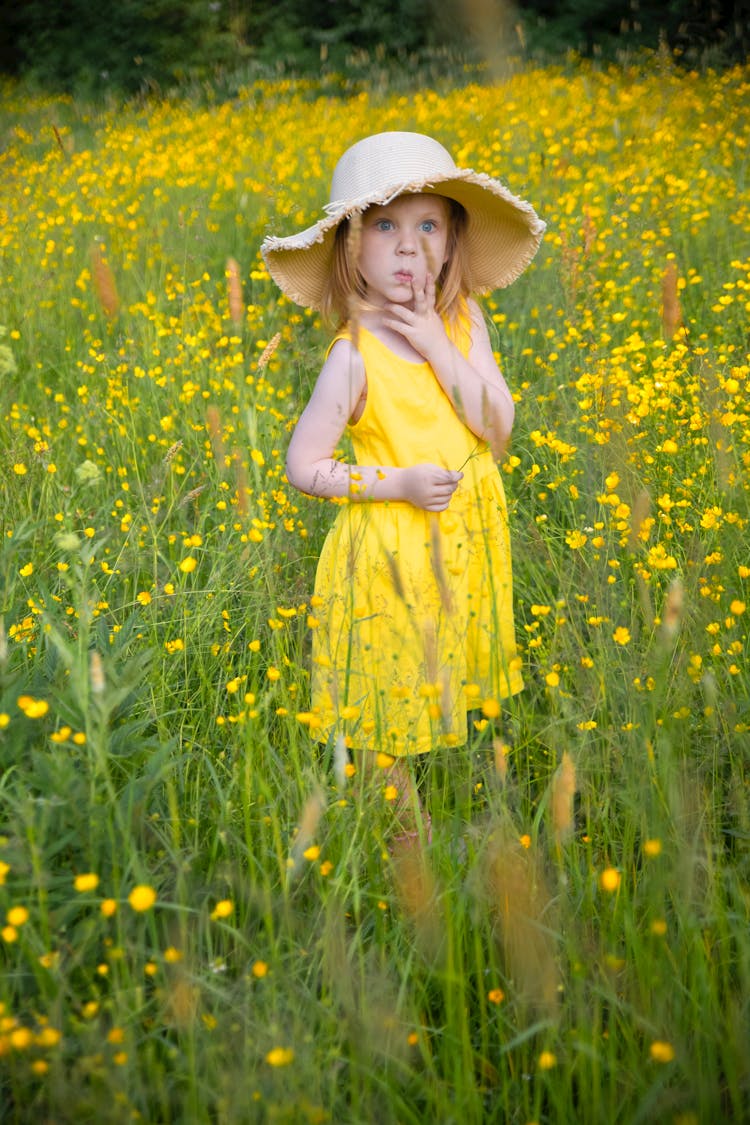 A Little Girl In A Yellow Dress And A Hat Standing On A Meadow With Yellow Flowers 