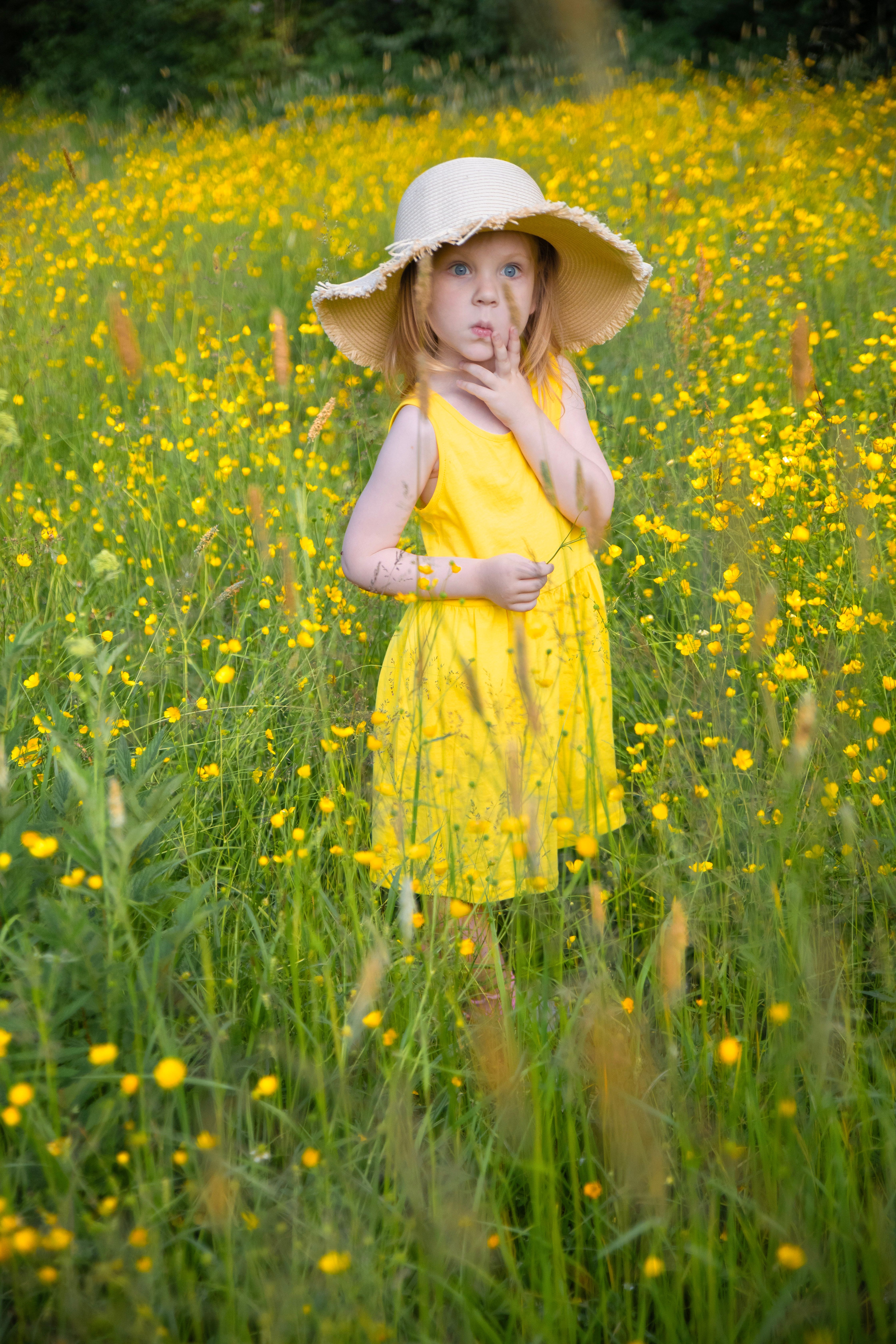 A Little Girl in a Yellow Dress and a Hat Standing on a Meadow with ...