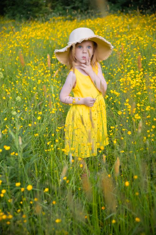 Free Adorable girl in a yellow dress with hat standing in a flower-filled meadow. Stock Photo
