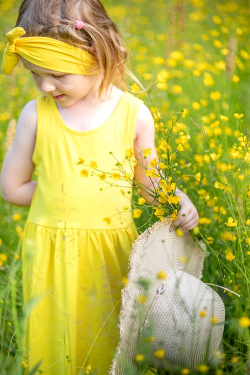 Free Young girl in a yellow dress holding a bouquet in a sunny meadow full of wildflowers. Stock Photo