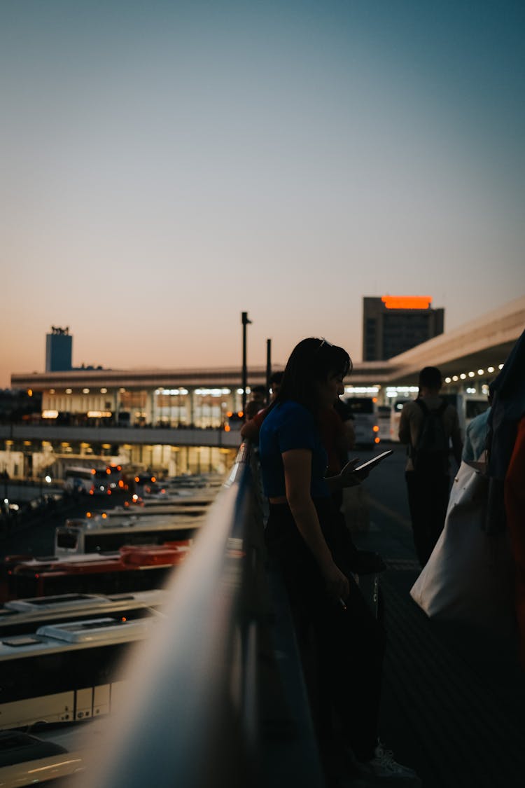 View Of People Standing On A Terrace At An Airport With Buses Parked Along The Building 