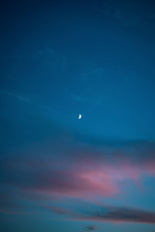 Free Vibrant crescent moon setting in a colorful evening sky with pink clouds and deep blue tones. Stock Photo