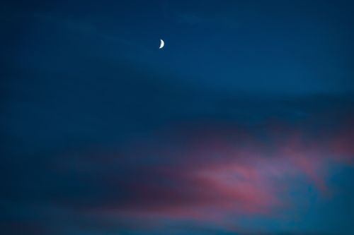 Free A serene crescent moon in a deep blue sky accented with soft pink clouds at twilight. Stock Photo