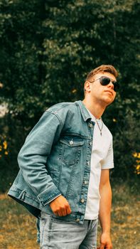 Stylish outdoor portrait of a young man in sunglasses and a jean jacket, exuding confidence.