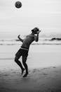 一张黑白照片中，一名男子正在海滩上踢足球