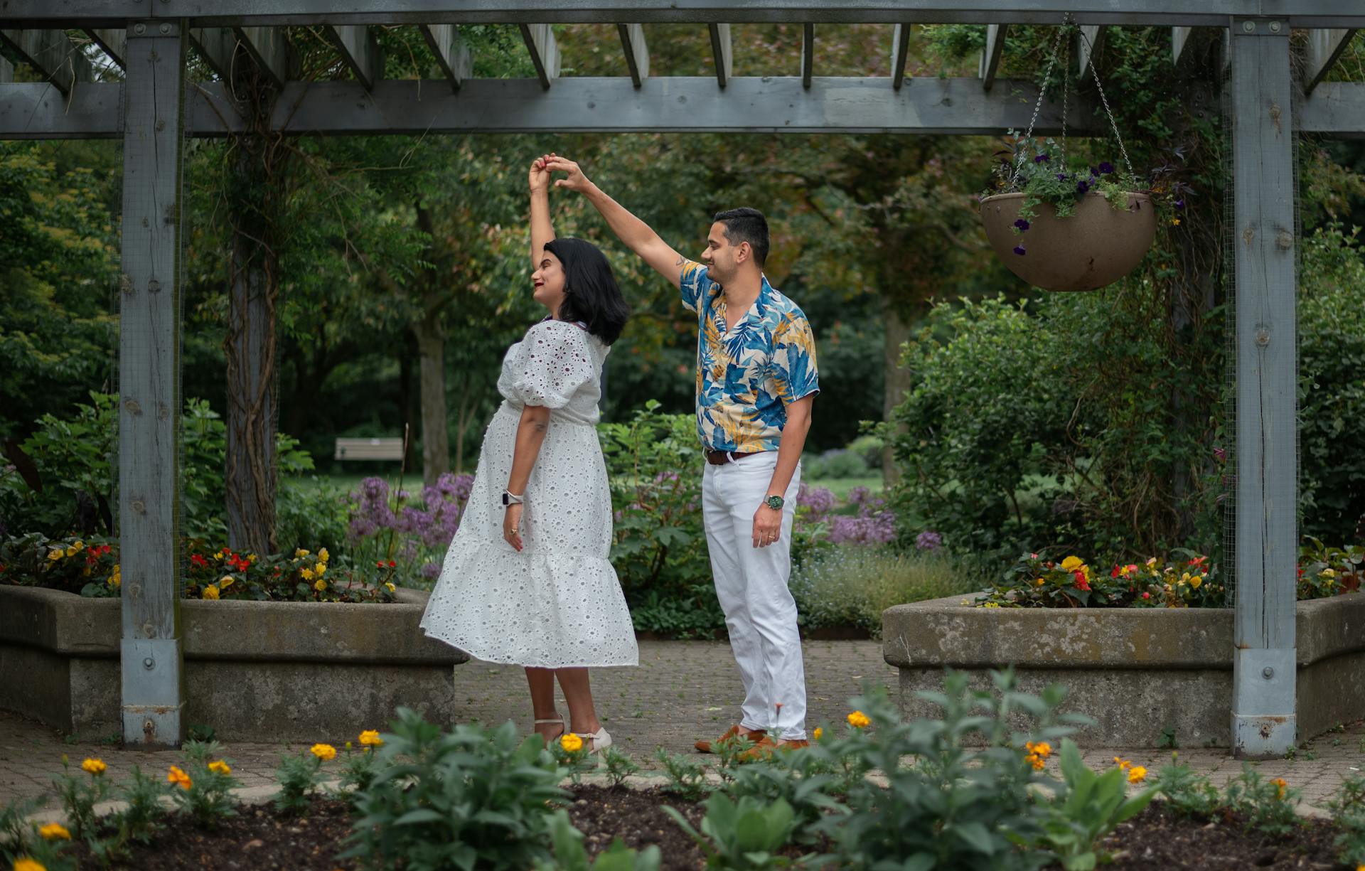 Couple shares a joyful dance beneath a pergola surrounded by vibrant flowers in a serene garden.