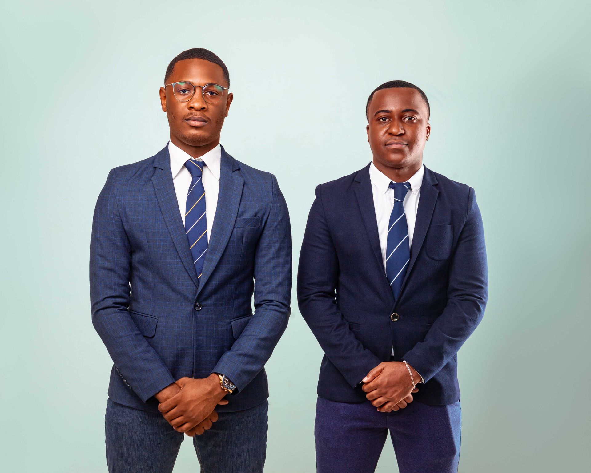 Two professional businessmen posing in formal suits against a neutral backdrop.