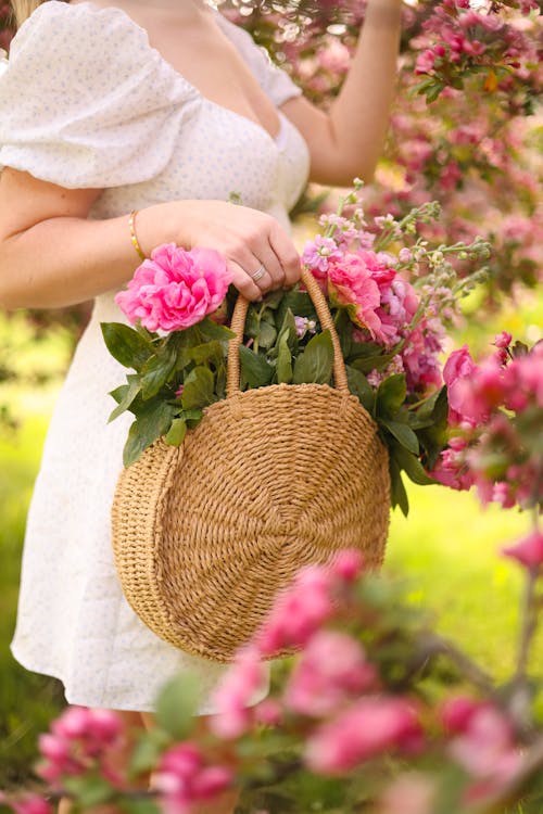 Woman Holding Flowers in the Basket and Standing in the Garden 