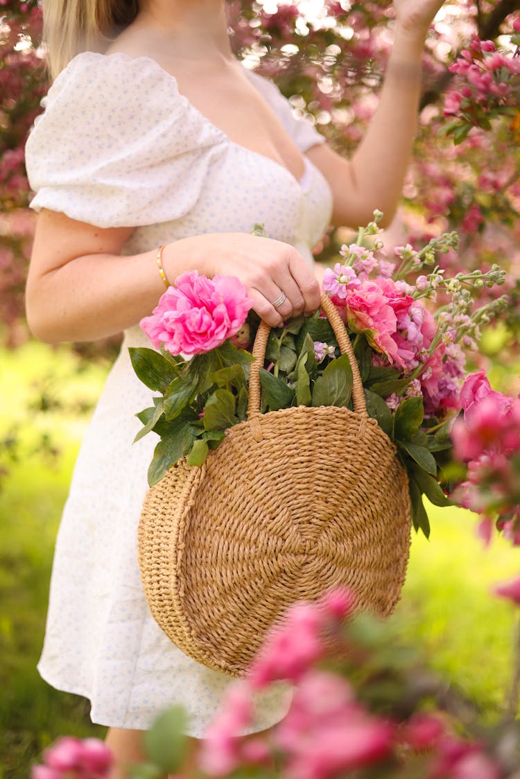 Woman Holding Flowers In The Basket And Standing In The Garden 