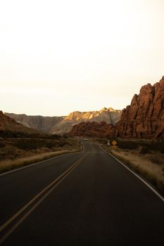 A deserted highway winding through rugged red rock formations at sunset.