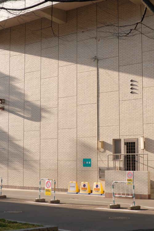 Free A serene city corner with a building facade, safety barriers, and sunlight casting shadows. Stock Photo