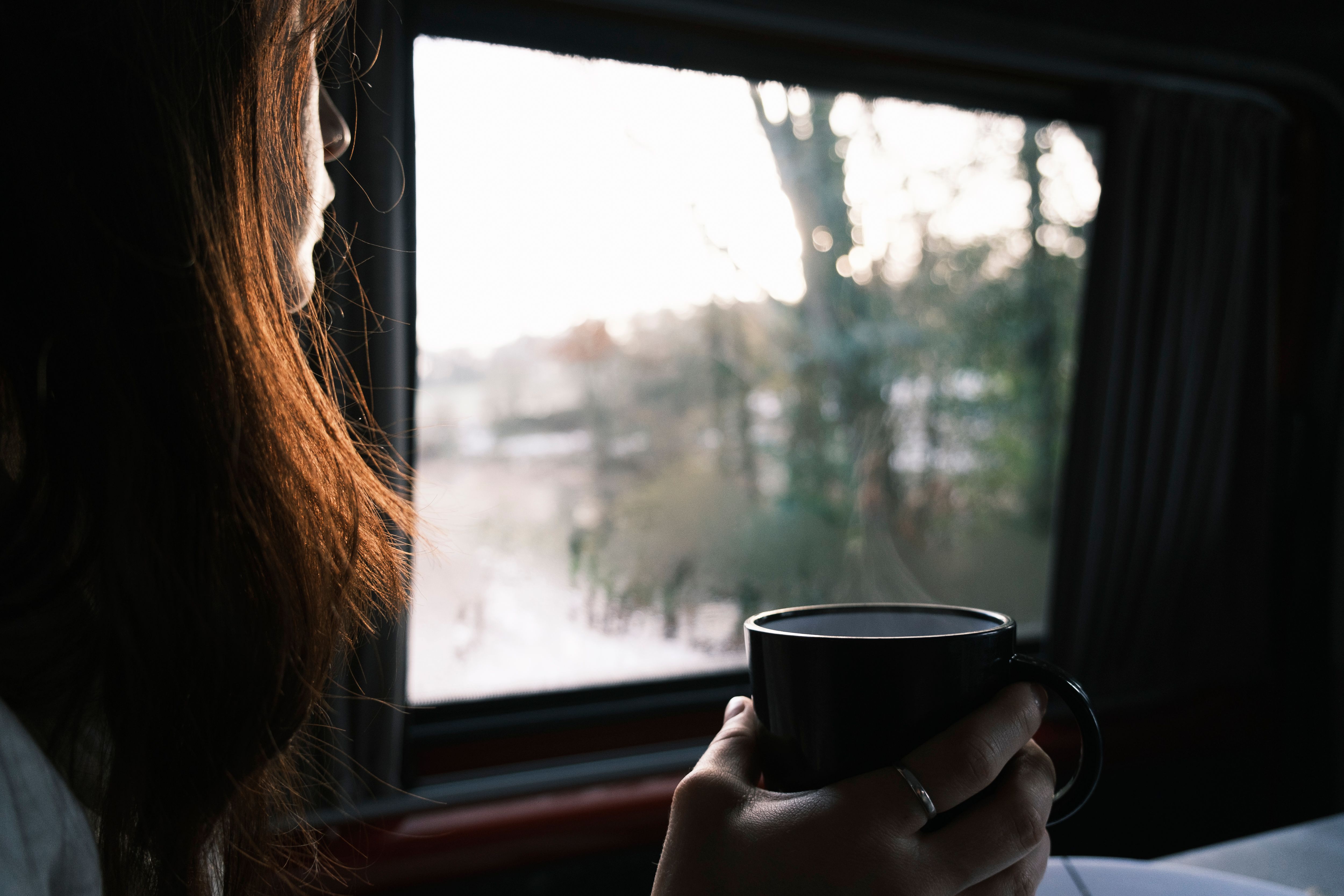 person sitting by window with morning light, holding a warm mug, looking calm and reflective
