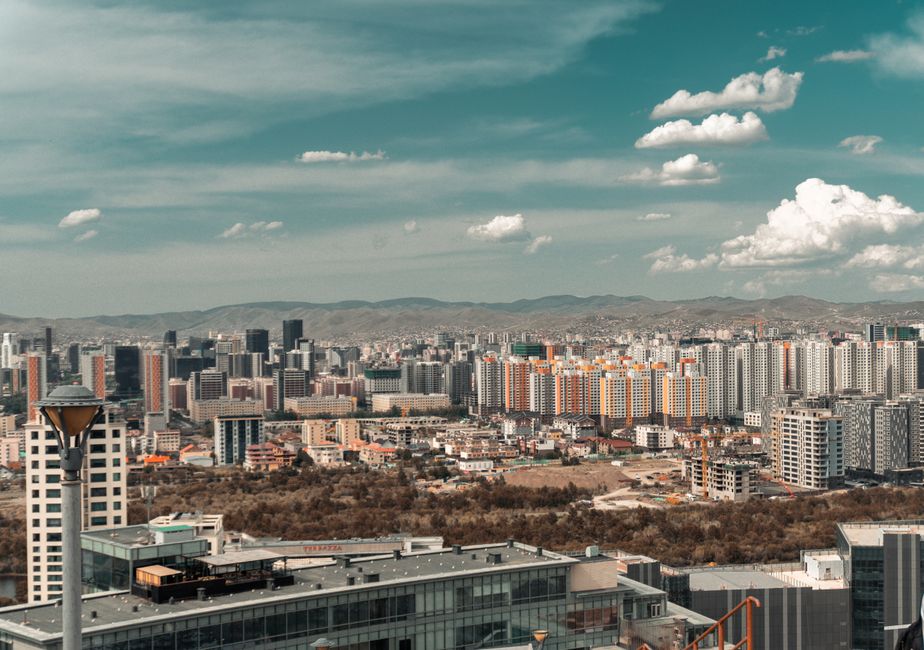 Aerial view of a modern city skyline under a vibrant blue sky with scattered clouds.