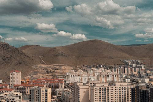 Free Aerial view of a sprawling cityscape with buildings set against a backdrop of hills under a cloudy sky. Stock Photo