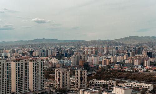 Free A wide-angle view of a sprawling modern city skyline with diverse architecture against a mountainous backdrop. Stock Photo