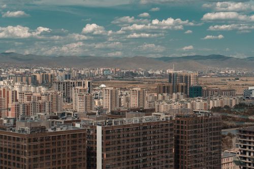 Free Expansive urban skyline with modern buildings and distant mountains under a blue sky. Stock Photo
