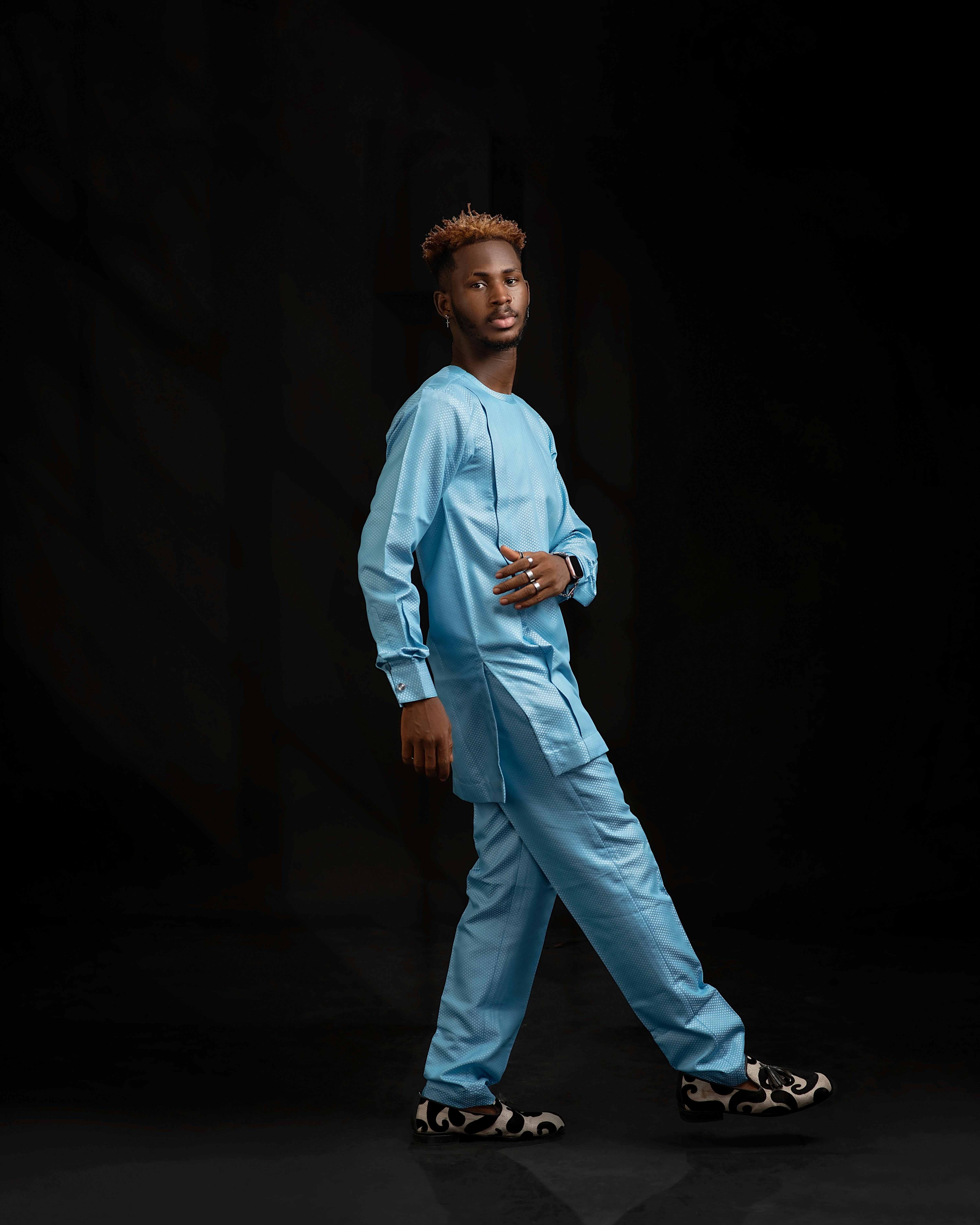 A fashion model poses in a striking blue traditional outfit against a dark background.