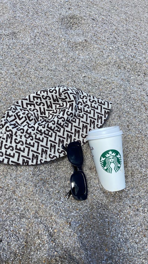 Disposable Cup next to a Hat and Sunglasses on a Beach 