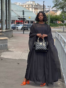 Stylish woman in black dress posing with designer bag on a street in Glasgow, showcasing elegant urban fashion.
