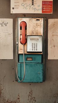 Vintage payphone with a red handset against a textured urban backdrop, evoking nostalgia.