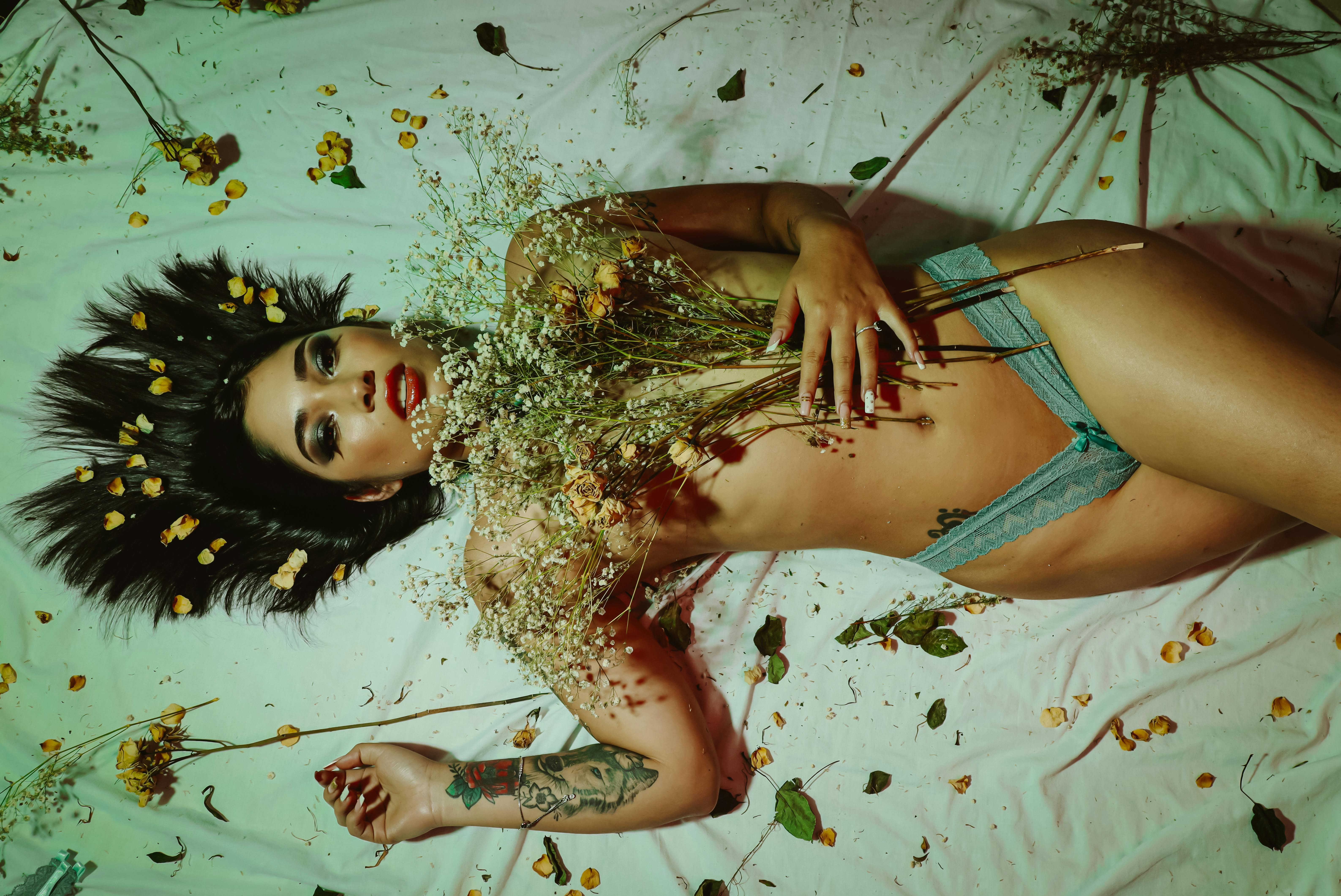 Top view of a woman lying on a bed surrounded by flowers, evoking a dreamy and artistic mood.