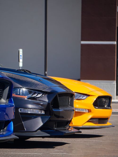 Free Three sports cars lined up in a sunlit urban environment, showcasing sleek design and vibrant colors. Stock Photo